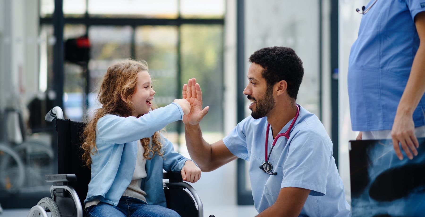 Clinician high-fiving a young patient in a wheelchair